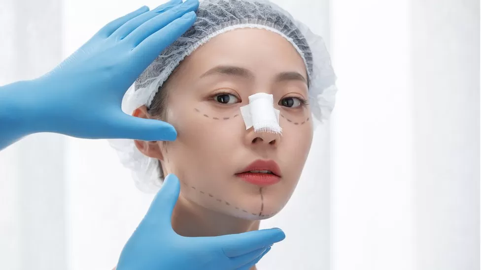 A doctor examining a patient's nose eyes and chin prior to facelift plastic surgery.